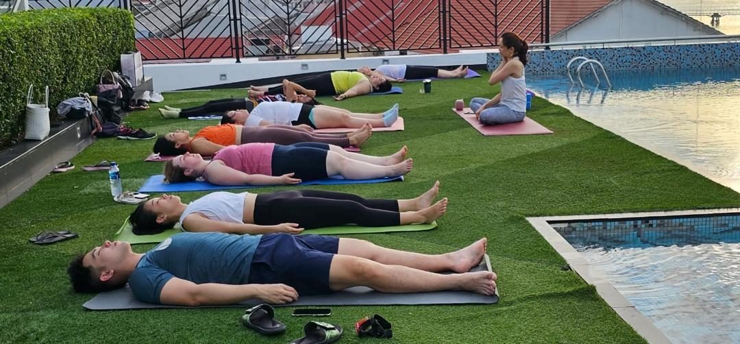 Class resting on mats on a rooftop lawn beside a pool